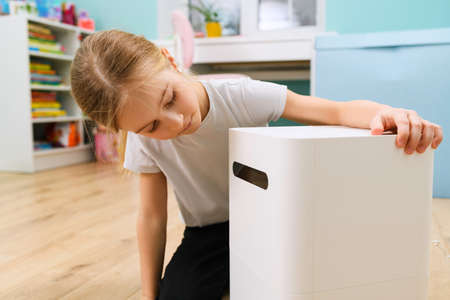 Small girl sitting at room floor and looking at big air humidifier device close up for comfort home stayingの写真素材