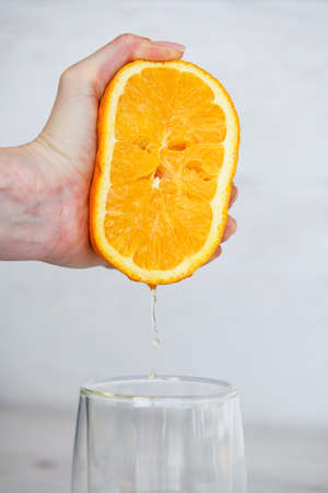Female hand squeezing half of fresh citrus orange juice under transparent glass, healthy breakfast natural drinkの写真素材