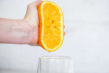 Female hand squeezing half of fresh citrus orange juice under transparent glass, healthy breakfast natural drinkの写真素材