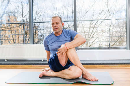 Middle age sportive man during workout training on floor mat in light studio, twirl and stretch body musclesの写真素材
