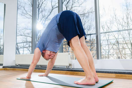 MIddle age man stay on floor mat, making workout yoga training in downward dog pose, tild and bend...