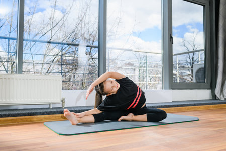 Small flexible sporty girl doing yoga fitness exercises at floor mat near panoramic window, healthy childhoodの写真素材