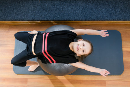 Smiling tween child gymnast girl exercise with gray rubber sportive gym ball and mat indoors, happy active childhoodの写真素材