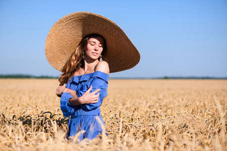 Adorable young girl in a wide-brimmed hat in a wheat field. Woman hugs herself.の写真素材