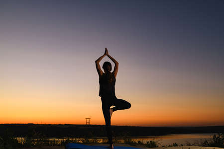 Female silhouette stand in tree yoga positon at sunrise horizon, find balance in healthy lifeの写真素材