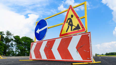 Road works sign on the road. Repair work of road signs and a bypass arrow on a background of blue sky.の写真素材