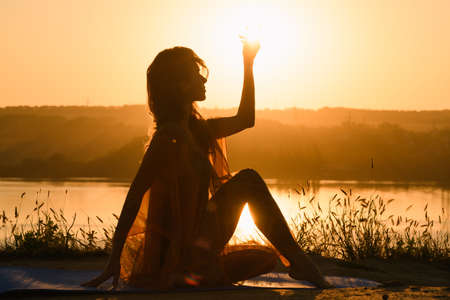 Female silhouette doing yoga against warm sunの写真素材