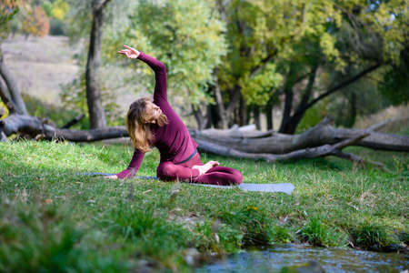 Fit woman sit in yoga lotus pose and stretch hands in scenic forest woods background, sport outdoorsの写真素材
