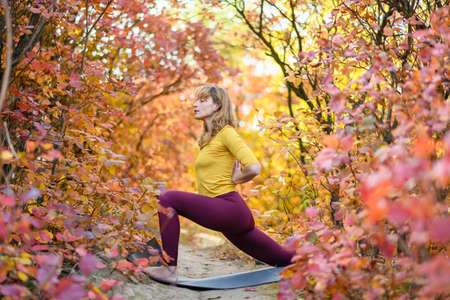 Woman middle age stand in side warrior yoga pose with namaste hands back in autumn fall colorful forestの写真素材