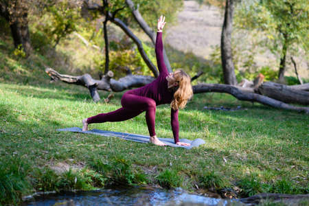 Woman stand barefoot on mat, stretching hands and legs in comfortable leggings at beautiful forest backgroundの写真素材