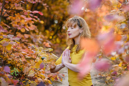 Portrait of woman meditate with closed eyes and hands in namaste at fall autumn forest background with colorful foliageの写真素材