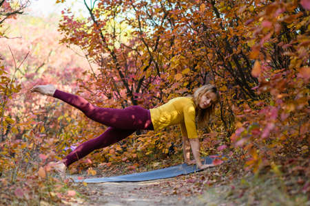 Woman barefoot stand on mat and making yoga fitness plank exercise in colorful autumn fall forest, healthy lifestyleの写真素材
