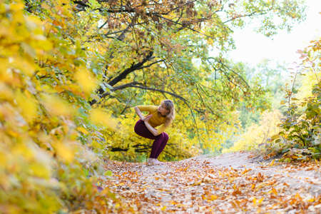 Woman exercise yoga balance posture with namaste hands at autumn forest barefoot, workout in scenic natureの写真素材