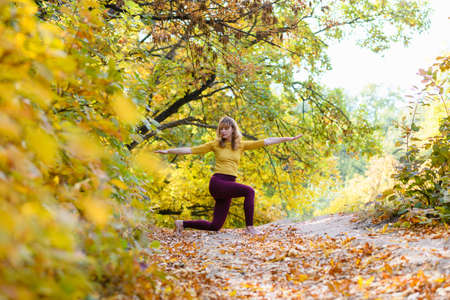 Woman middle age exercise yoga warrior pose at autumn scenic forest with colorful leaves, close to nature, healthy lifeの写真素材