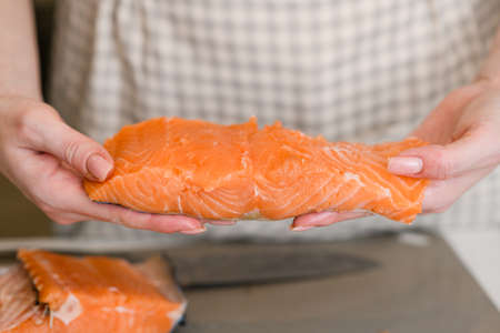 Fillet of raw red salmon fish in Caucasian woman hands, close up. Woman in apron holding a piece of red fish.の写真素材