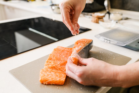 Female hands salt red fish fillets in the kitchen.の写真素材