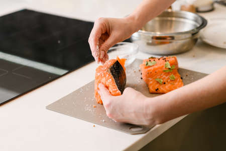 Cooking lightly salted red fish. Woman salting fresh raw salmon at table, closeup.の写真素材