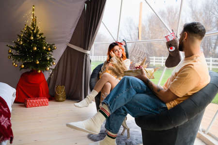 Young couple are sitting in a cozy glamping. The man gives a gift to the woman for Christmas.の写真素材