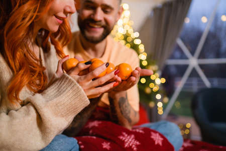 Young couple with tangerines while sitting on bedの写真素材