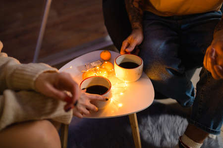 Close-up of two cups with coffee on the table. The glowing garland lies on the table next to the cups and tangerines.の写真素材