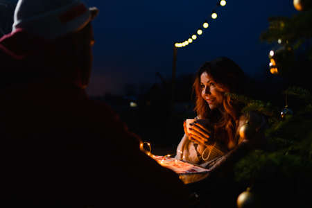 Girl with a cup of hot drink sits outdoors by the Christmas treeの写真素材