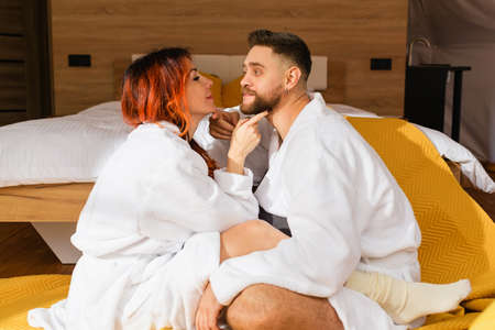 Young loving couple cuddling sitting face to face on the floor near the bed in the hotel.の写真素材