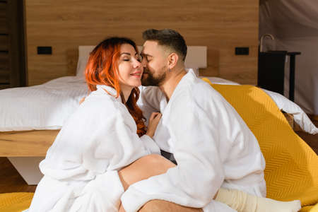 Young loving couple cuddling sitting face to face on the floor near the bed in the hotel.の写真素材
