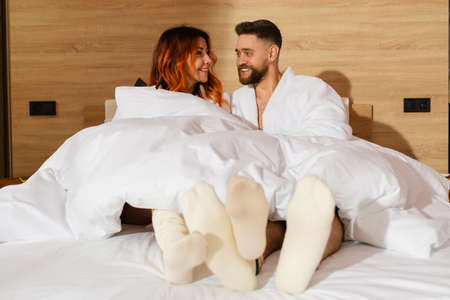 A young couple, a man and a woman, are lying in bed dressed in white bathrobes.の写真素材