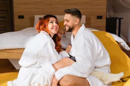 Young loving couple cuddling sitting face to face on the floor near the bed in the hotel.の写真素材
