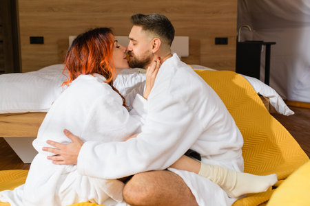 Young loving couple cuddling sitting face to face on the floor near the bed in the hotel.の写真素材