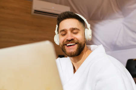 Young handsome bearded man with headphones and laptop. Close-up. Man closed his eyes and smiles.の写真素材