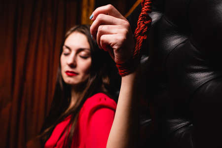 Bondage woman tied to bed with red ropes. Close-up of a woman's hand tied to the bed.の写真素材