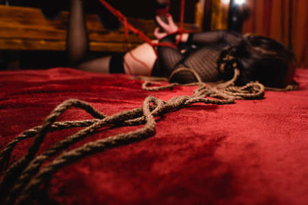 A close-up of a shibari rope. The figure of a tied woman lying on a bed with her hands behind her back. high quality photoの写真素材