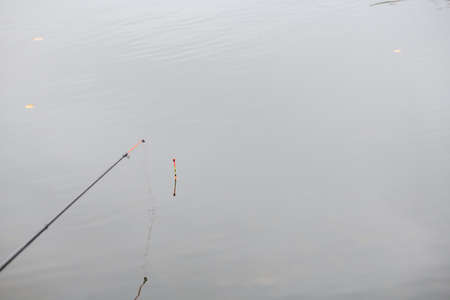Fishing rod and float in the calm water of an autumn lake or river. high quality photoの写真素材