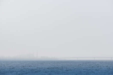 Silhouette of a factory and a bridge over a river or sea in the fog. Foggy day in the bay. High quality photo.の写真素材