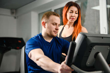 Female trainer teach man to use equipment machines at modern gym, look at screen together, start workout training exercisesの写真素材