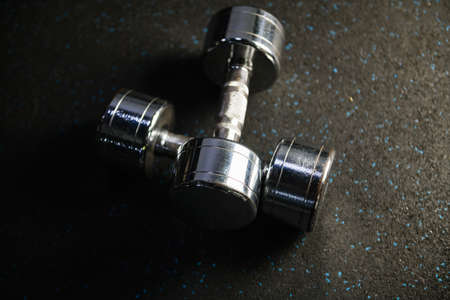 Two shining metal dumbbells weights at gym rubber carpet close up, sport fitness equipment for healthy lifestyle and body-buildingの写真素材