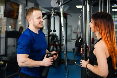 Woman customer talking with sport trainer coach at modern gym hall interior for workout exercises...