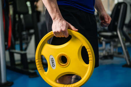 Strong muscular man hands with lifting yellow round heavy weight disk for dumbbell in gym, healthy sportive lifestyleの写真素材