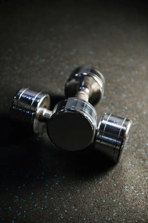 Two shining metal dumbbells weights at gym rubber carpet close up, sport fitness equipment for healthy lifestyle and body-buildingの写真素材