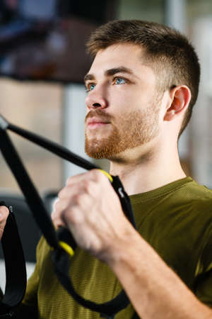 Young man portrait during gym exercises, fit handsome male workout for strong hands with modern equipment indoorsの写真素材