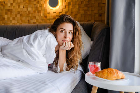 Attractive young woman having breakfast in bed in the morning