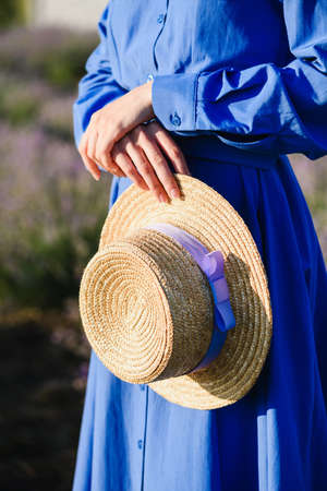Woman holding a straw hat with purple ribbon in hands.の写真素材
