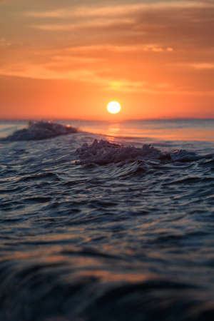 Focus on stormy sea surface with water splashes and foam at orange dramatic sky landscape, vertical...
