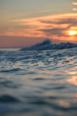 Close-up of the sea surface against the sunset. Vertical photo, low shooting point. Sea waves in the foreground.の写真素材