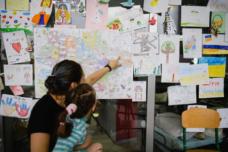 Dnipro, Ukraine - April 04, 2022: A mother point her daughter a house on a map of Ukraine, from where they were forced to flee the war.のeditorial素材