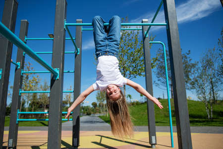 Little funny girl with long hair hanging upside down on the horizontal bar. Bottom view, wide angle.の写真素材