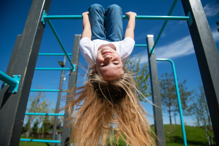A beautiful teenage girl hanging upside down on the horizontal bar. Hair is blowing in the wind. Bottom view, wide angle.の写真素材