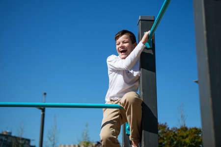 A teenager boy sits on a horizontal bar. bottom view. Sky in the background.