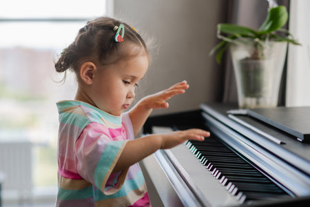 A beautiful little asian girl plays the piano in the living room or music school. Preschool child having fun learning to play a musical instrument. The concept of education, skills.の写真素材